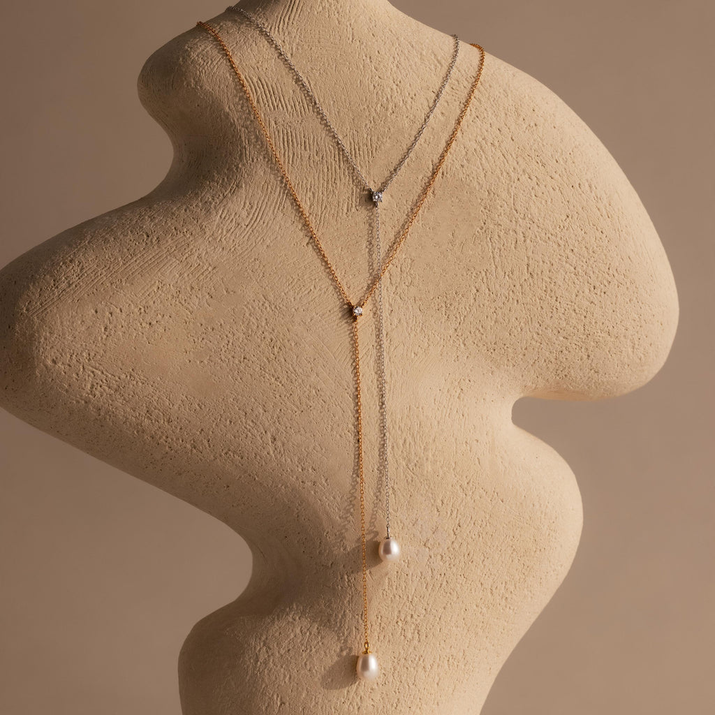 The Pearl Drop Lariat Necklace is elegantly displayed on a textured, abstract mannequin bust, showcasing its delicate design.