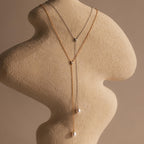 The Pearl Drop Lariat Necklace is elegantly displayed on a textured, abstract mannequin bust, showcasing its delicate design.