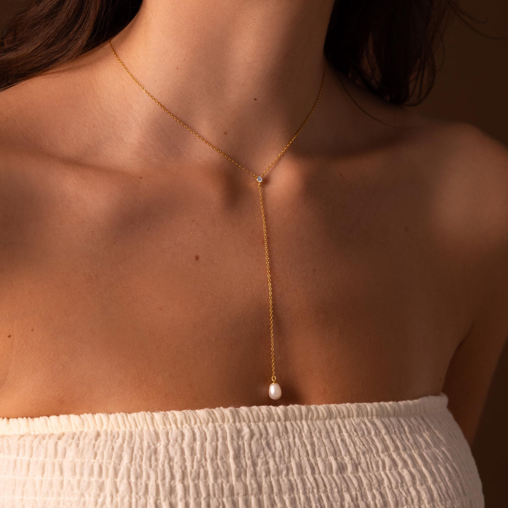 A woman wearing a delicate vertical chain, the Pearl Drop Lariat Necklace in 18K Gold, showcases her taste for elegant jewelry.