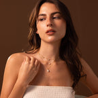A woman with long brown hair wears the Pearl Dot Necklace layered with gold chains and a white strapless top, gazing to the side.