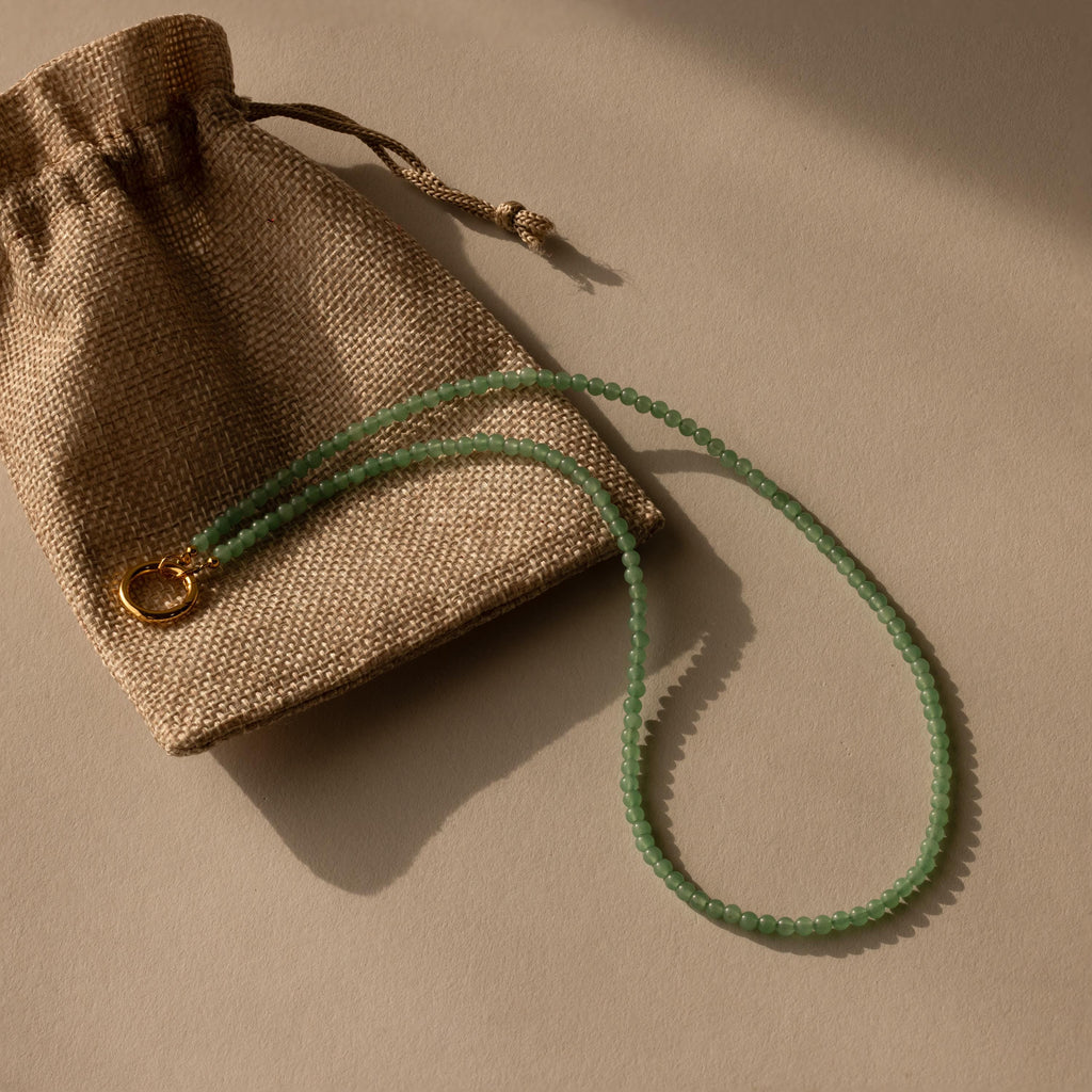 Beaded Jade Clasp Necklace in 18K Gold, ideal for layering, displayed on a brown burlap pouch with a beige background.