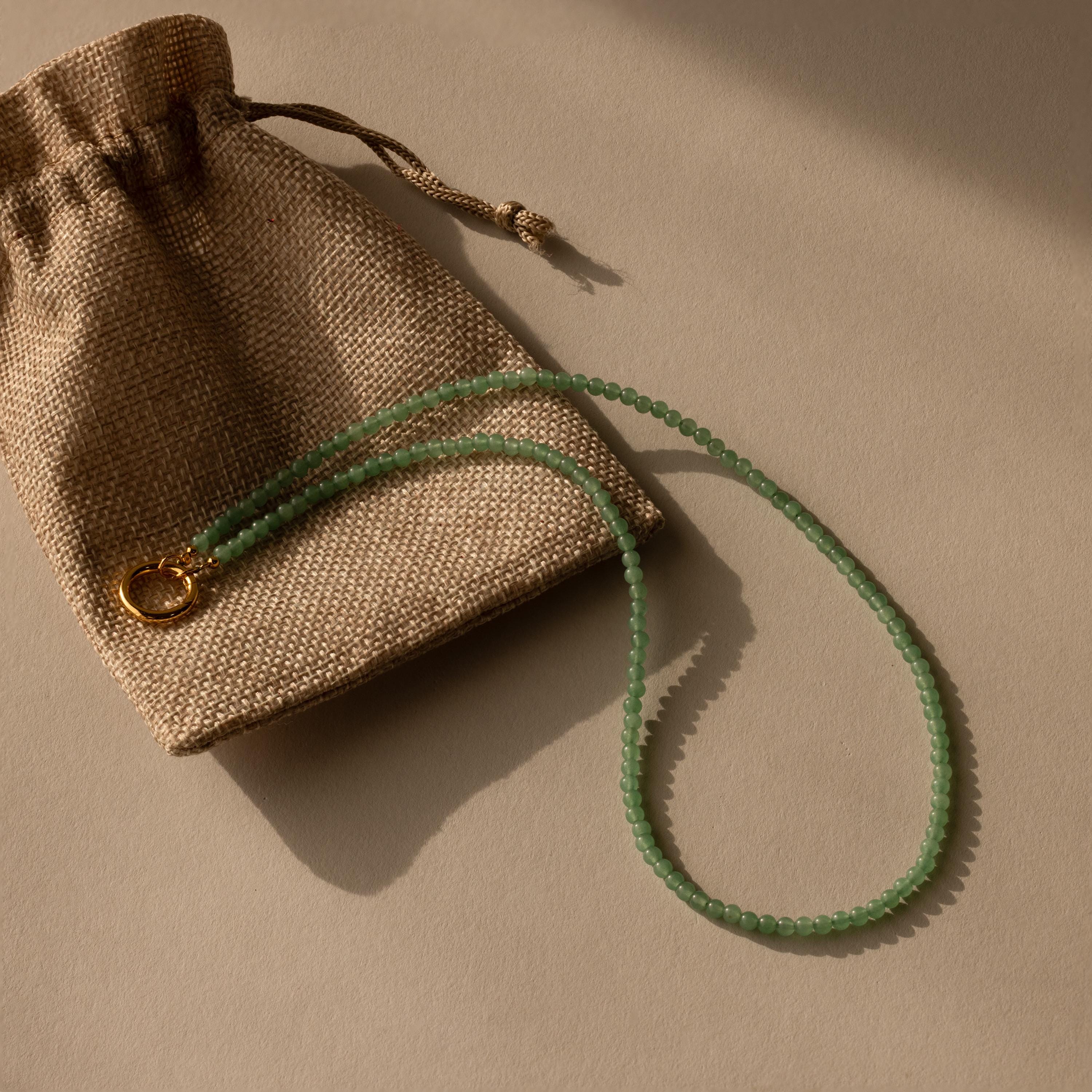 Beaded Jade Clasp Necklace in 18K Gold, ideal for layering, displayed on a brown burlap pouch with a beige background.