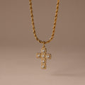 The Majesty Cross Necklace in 18K Gold features a diamond-studded cross pendant on a gold rope chain, ideal as faith jewelry, shown against a neutral brown background.
