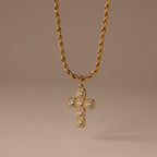 The Majesty Cross Necklace in 18K Gold features a diamond-studded cross pendant on a gold rope chain, ideal as faith jewelry, shown against a neutral brown background.