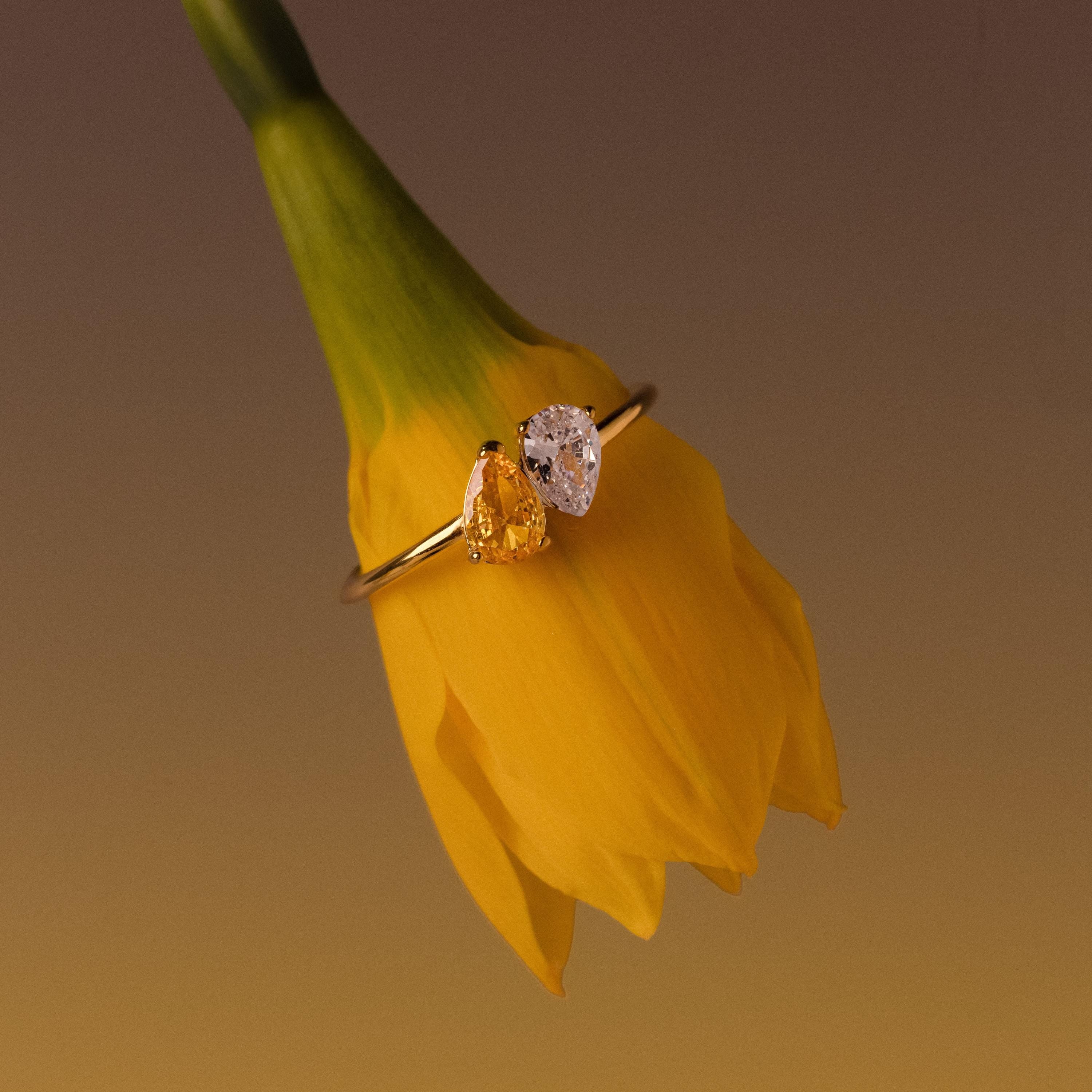 The Duo Pear Toi Et Moi Ring in 18K Gold, featuring two pear-shaped stones, rests on the yellow petals of a daffodil flower.