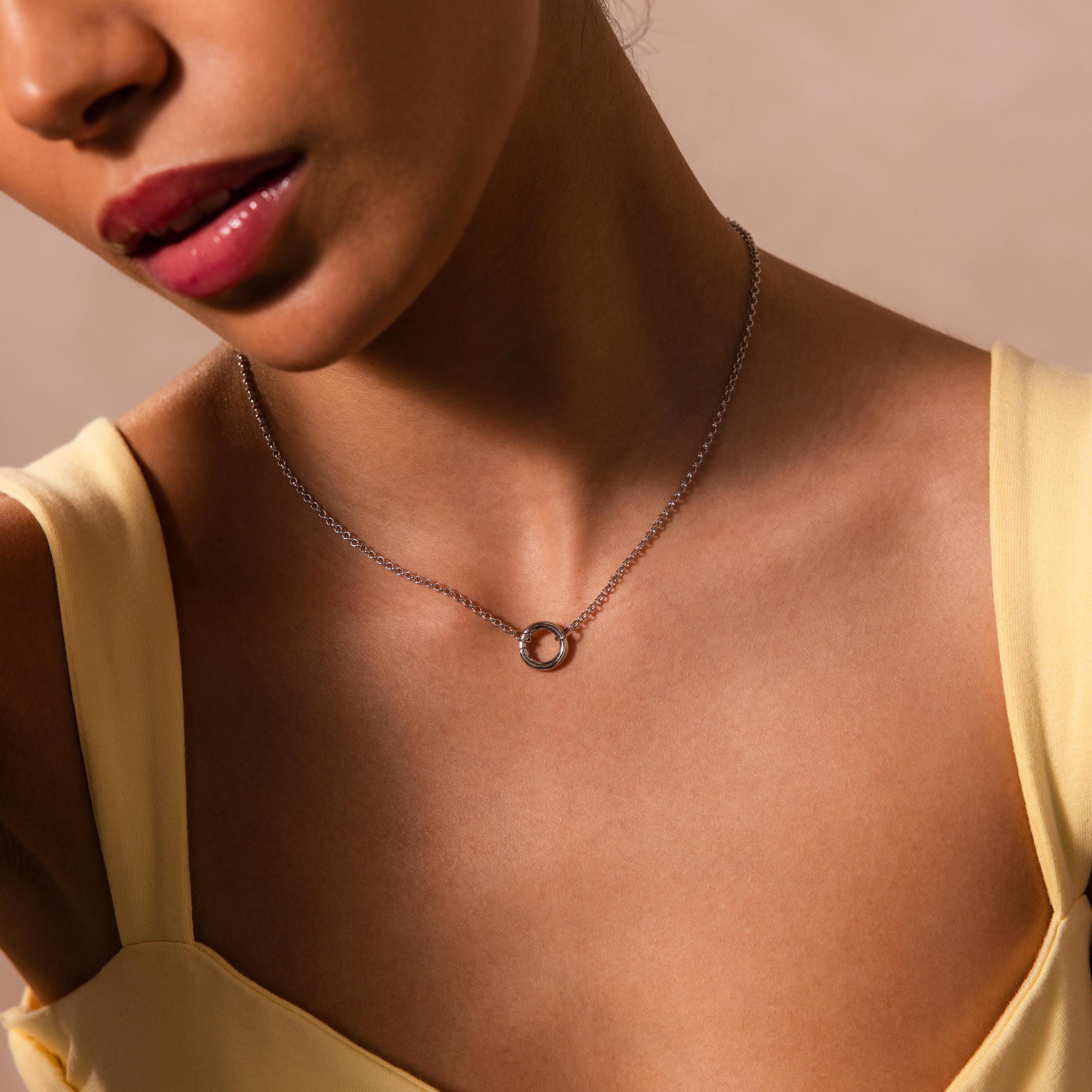 A woman in a yellow top wears the Cable Circle Charm Necklace in Silver, featuring a circular charm—a perfect statement piece to elevate any layered necklace style.