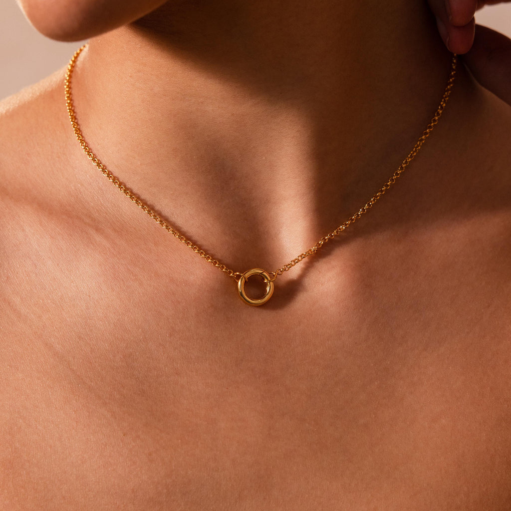 The Cable Circle Charm Necklace features a gold circular pendant, ideal for wearing on bare skin as a subtle layering piece or as a chic statement accessory.