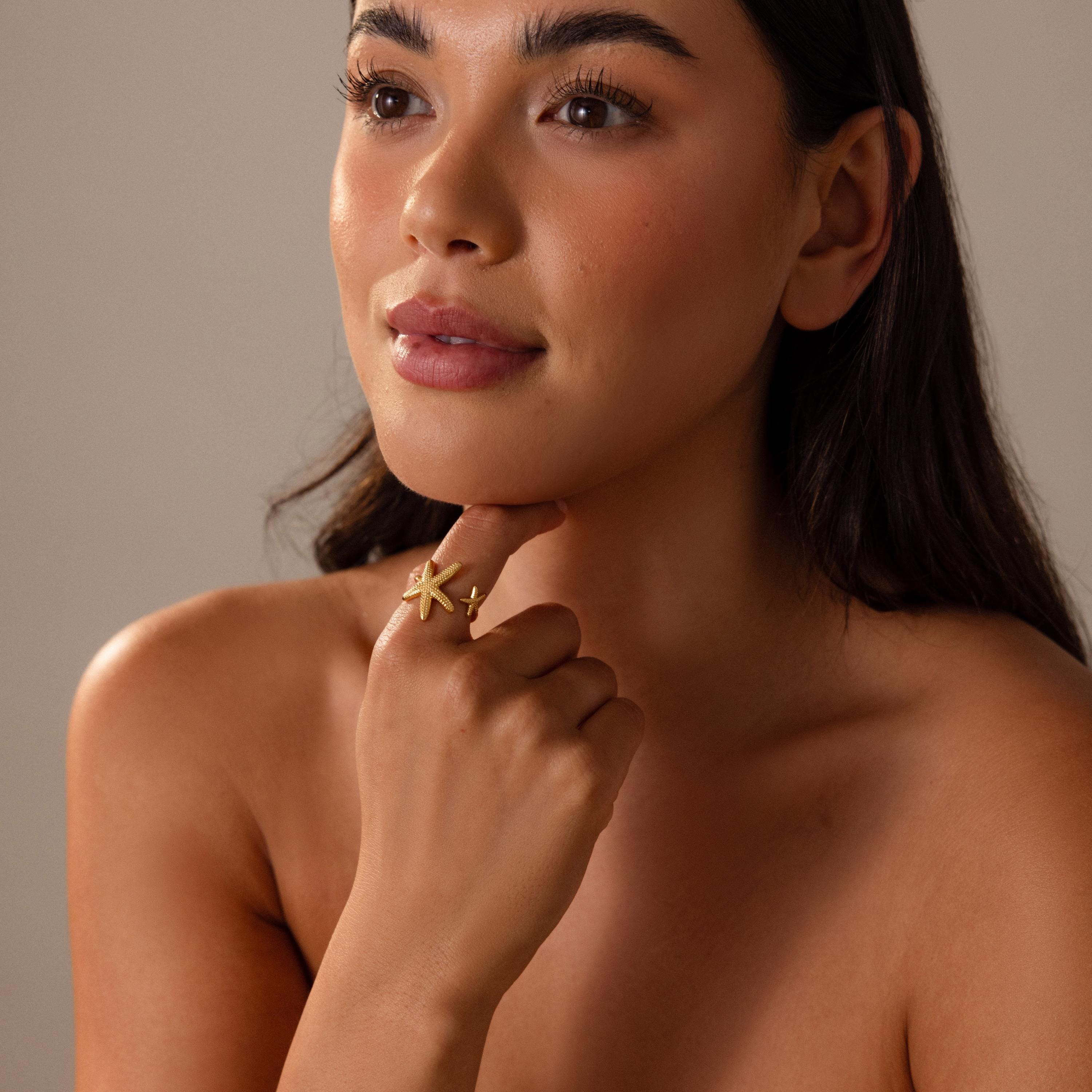 A woman with long dark hair poses thoughtfully with her hand on her chin, wearing the Open Duo Starfish Ring inspired by coastal style.