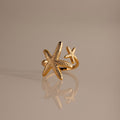 The Open Duo Starfish Ring showcases two textured starfish, one large and one small, on a reflective beige surface—a stunning gold coastal-inspired statement jewelry piece.