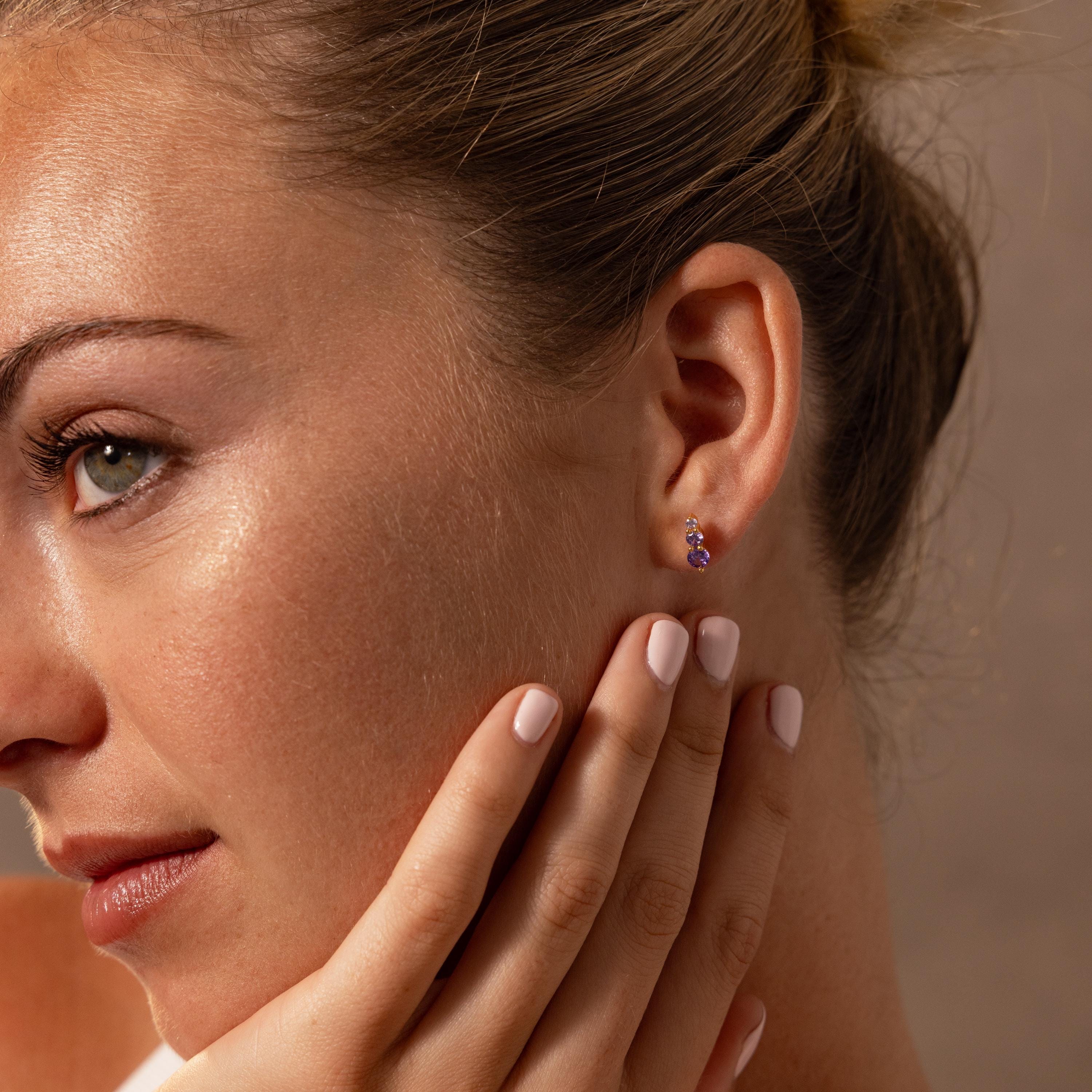 Woman with light skin and green eyes wearing Ombre Birthstone Flatback Studs, touching her face gently—a perfect choice for a personalized gift.