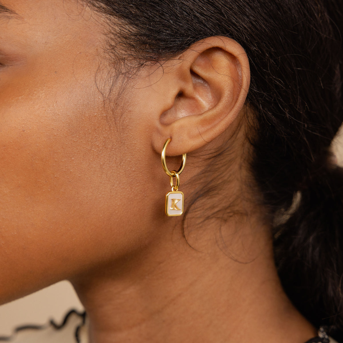 Close-up of an ear wearing a gold hoop earring with a 'K' charm.