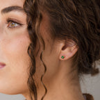 A close-up side profile of a woman with brown hair wearing a small green four-leaf clover stud earring.