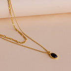 A gold layered necklace with a small oval black onyx pendant, displayed on a soft beige background.