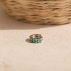 Our Garden Green Opal Huggies in silver resting on a light beige stone surface with a blurred woven basket in the background.