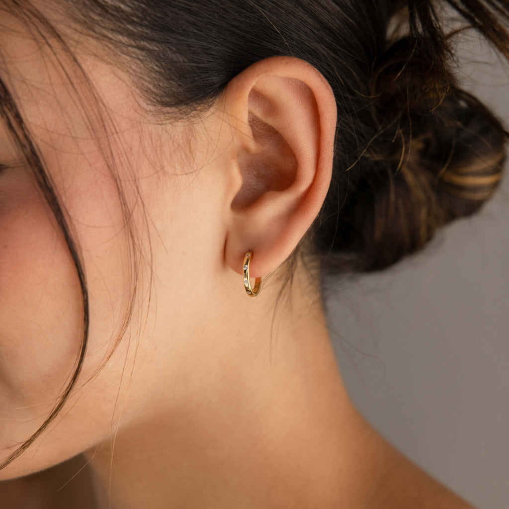 Close-up of a person wearing a gold hoop earring with a neutral background