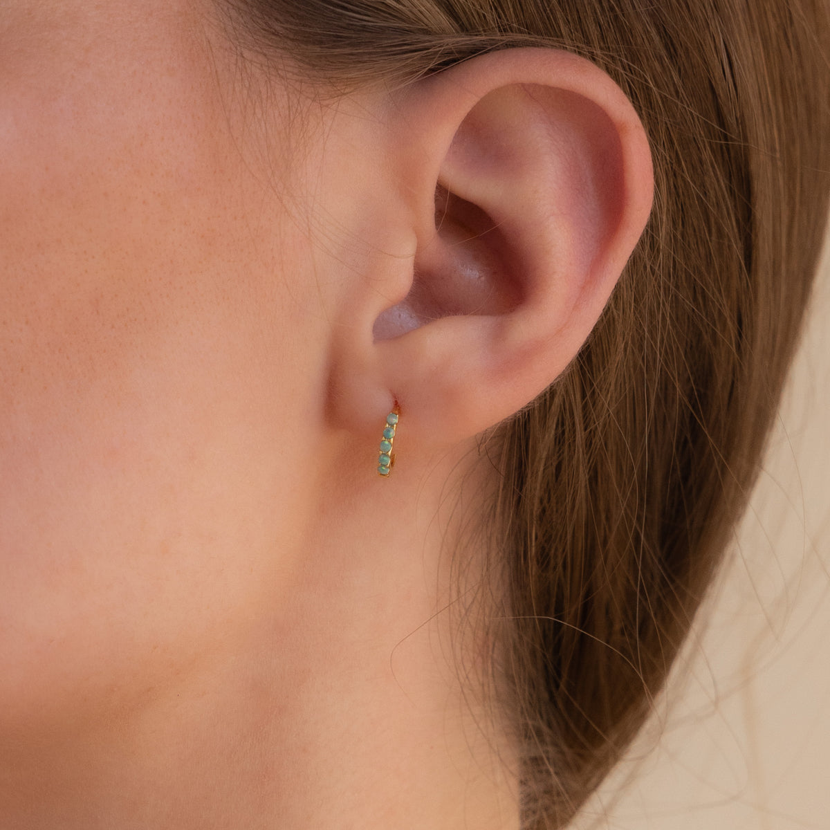 Close-up of an ear wearing our Garden Green Opal Huggies earring with a blurred background