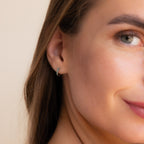 A close-up of a woman's ear wearing our Garden Green Opal Huggies earring against a soft beige background.