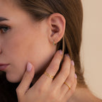 Close-up of a woman wearing our Garden Green Opal Huggies styled with two gold rings