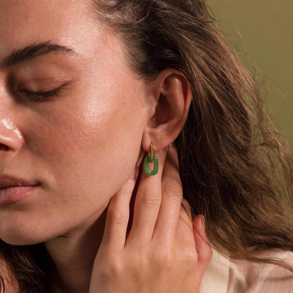 Woman wearing a gold hoop earring with a green jade link drop.