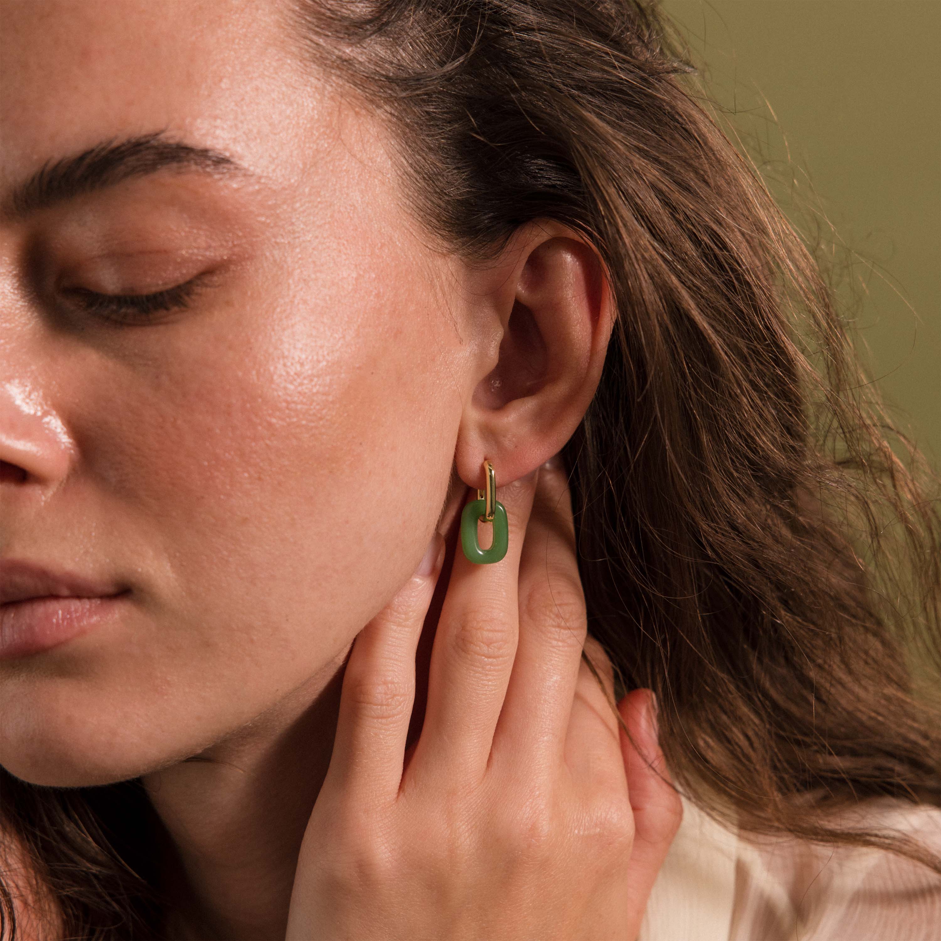 Woman wearing a gold hoop earring with a green jade link drop.