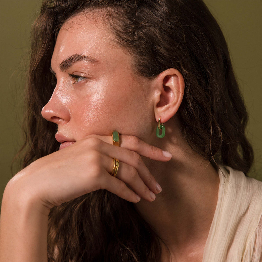 Woman wearing modern gold hoop earrings with rectangular jade link drops.