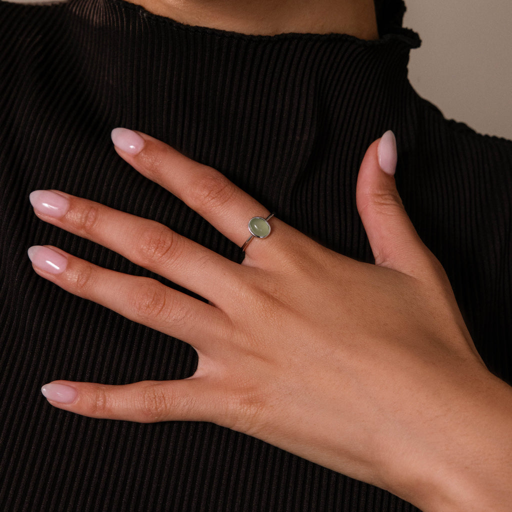 Close up of a model wearing a silver oval green gemstone ring with a thin polished band, styled against a black ribbed top for an elegant everyday jewelry look.