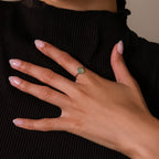 Close up of a model wearing a silver oval green gemstone ring with a thin polished band, styled against a black ribbed top for an elegant everyday jewelry look.