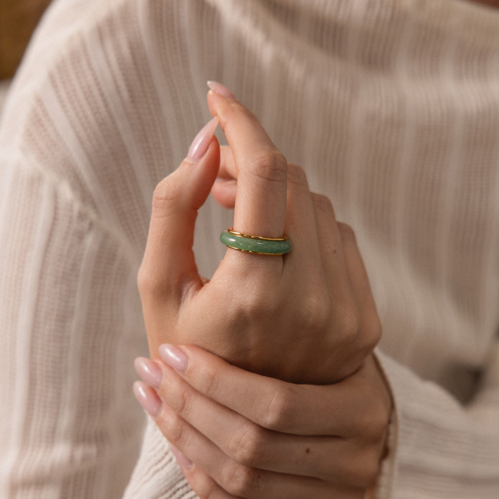 A hand with manicured nails wears the Haven Jade Spinner Ring, spinning the mindful jewelry with the other hand.