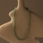 The Jade Choker Necklace in Silver is displayed on a textured, abstract beige bust set against a brown background.