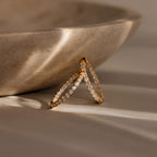 The Inside Out Diamond Hoops in 18K Gold, featuring sparkling diamonds and a timeless huggie design, are displayed against a beige stone bowl in gentle sunlight.