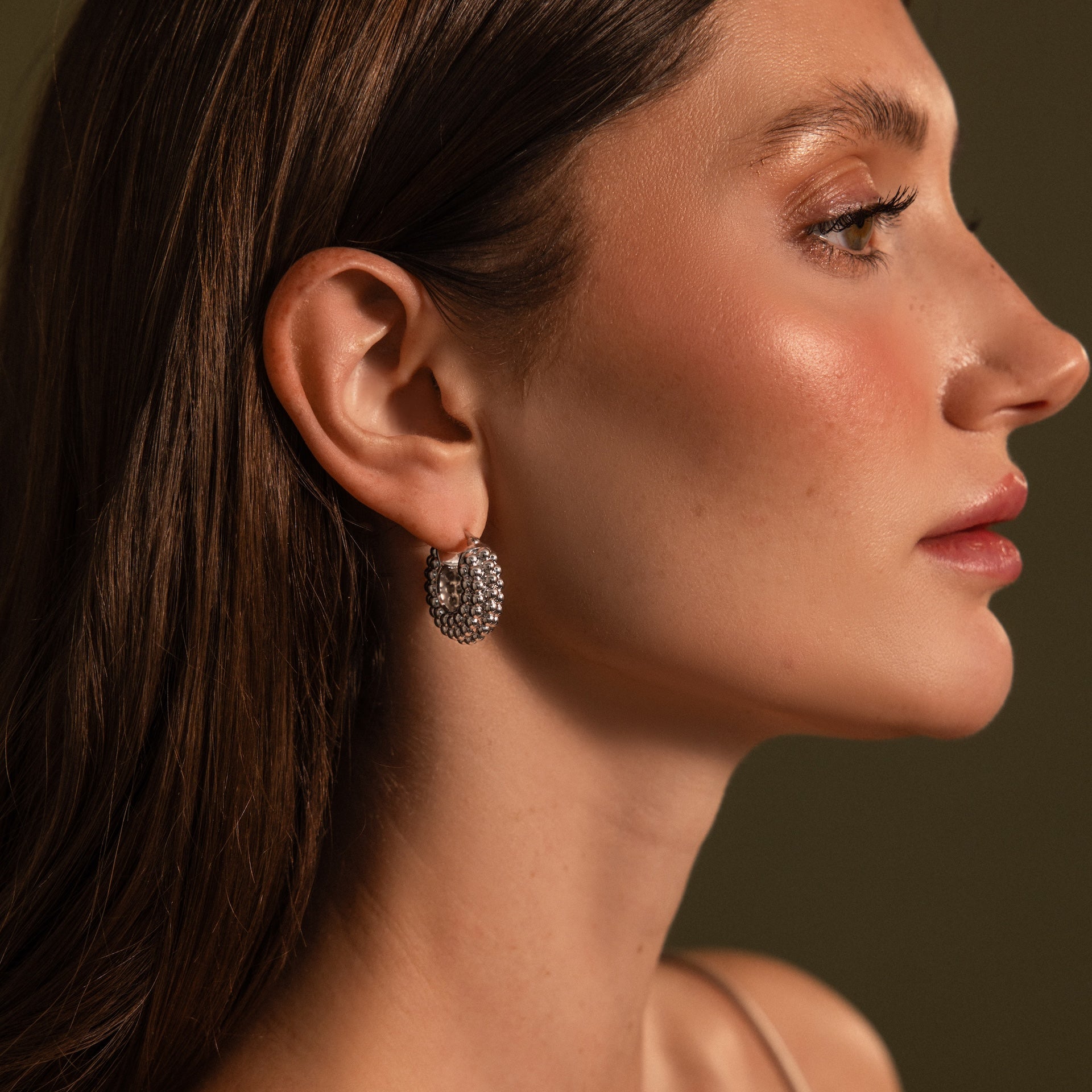Woman with long brown hair wears Beaded Dome Hoops in Silver, shown in profile against a neutral background.