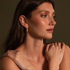 Woman with long brown hair wears Beaded Dome Hoops in 18K Gold, looking to the side with her hands resting on her shoulders.