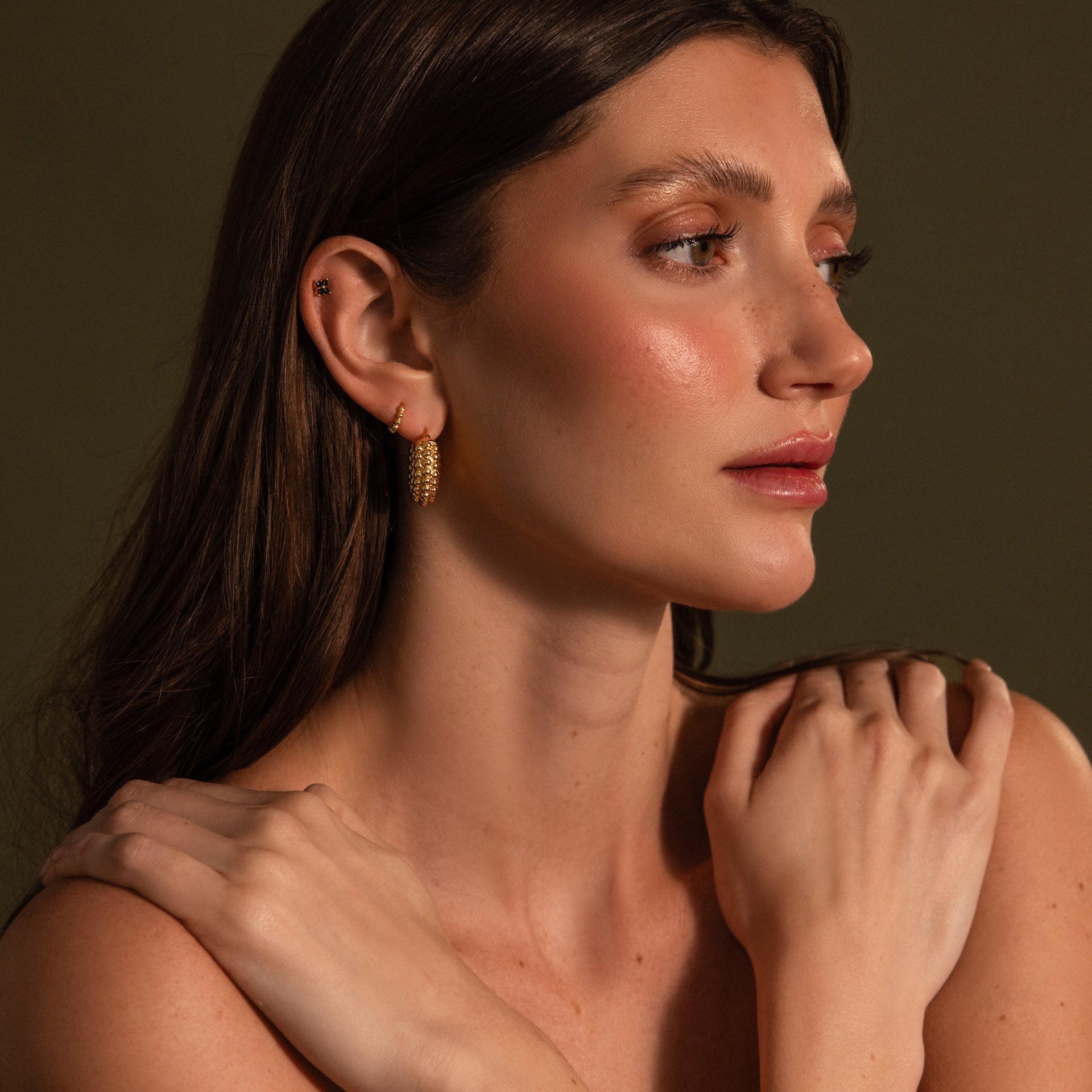 Woman with long brown hair wears Beaded Dome Hoops, posing with arms crossed against a dark background.