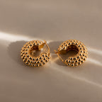 Beaded Dome Hoops in 18K Gold rest on a neutral surface, softly lit to highlight their textured gold beading and bold statement design.