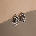 A pair of Beaded Dome Hoops in Silver showcased against torn beige paper.
