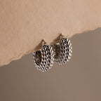A pair of Beaded Dome Hoops in Silver showcased against torn beige paper.