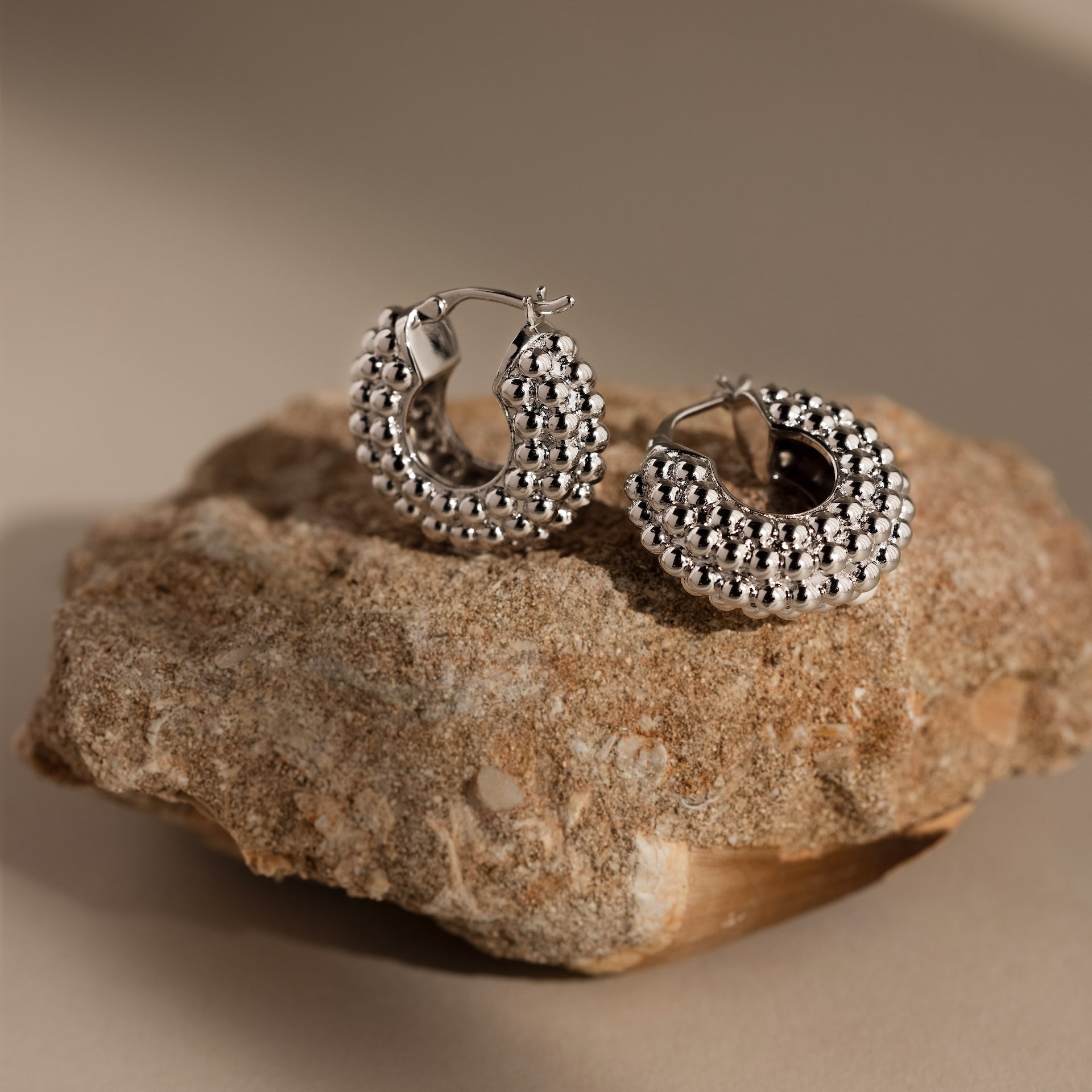 Beaded Dome Hoops in Silver, featuring subtle beading, are displayed on textured stone with a neutral background for a modern statement look.