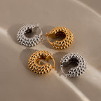 Two pairs of statement hoops, including Beaded Dome Hoops in gold and a silver style, are displayed on a soft beige fabric background.