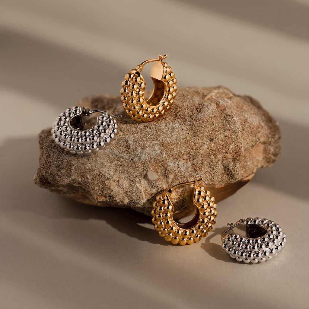 Beaded Dome Hoops are displayed on and beside a rough brown stone, featuring delicate gold beading for extra charm.