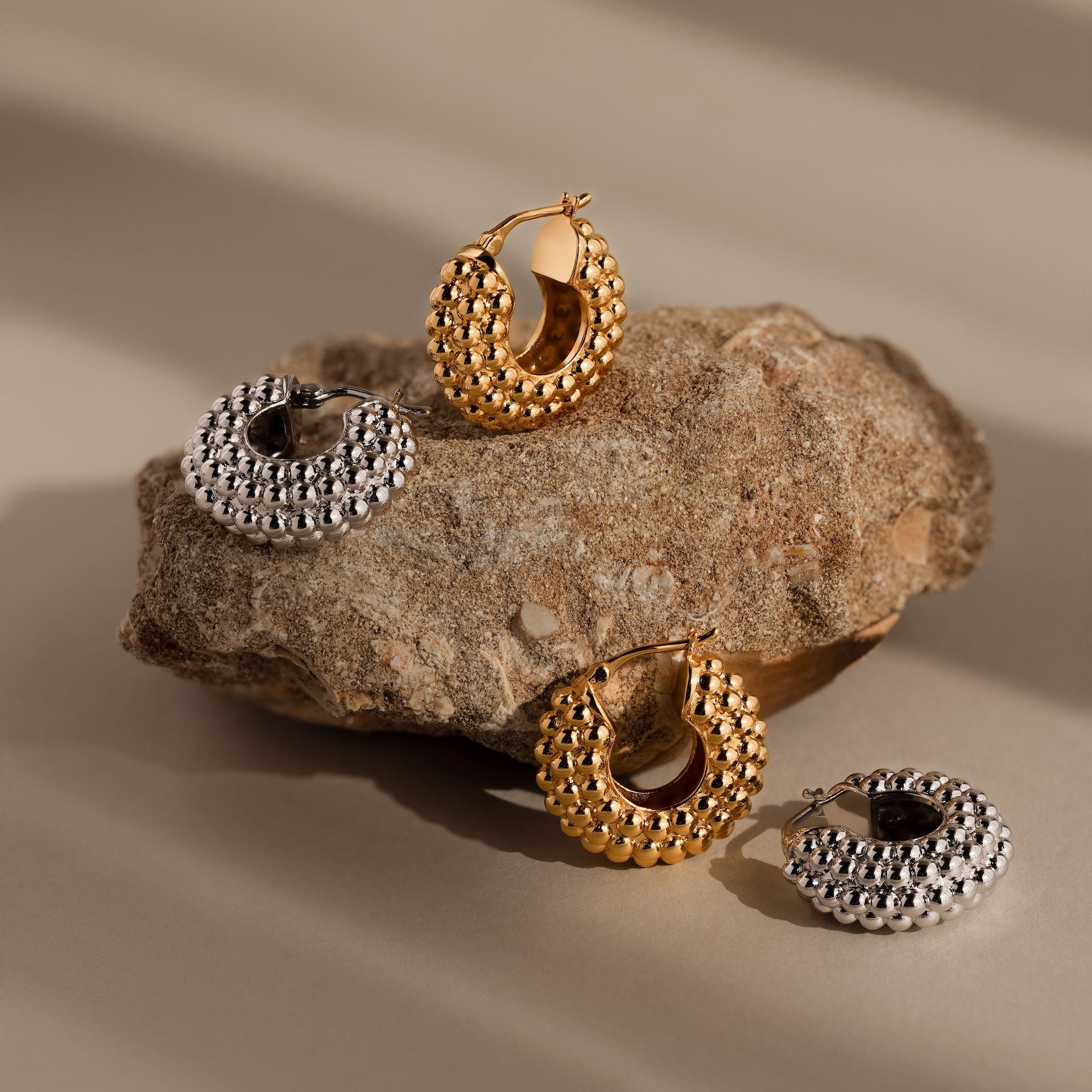 Beaded Dome Hoops are displayed on and beside a rough brown stone, featuring delicate gold beading for extra charm.