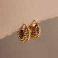 The Beaded Dome Hoops in 18K Gold feature intricate gold beading and are displayed elegantly against a neutral beige background for a refined touch.