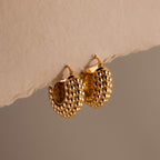 The Beaded Dome Hoops in 18K Gold feature intricate gold beading and are displayed elegantly against a neutral beige background for a refined touch.