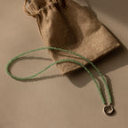 The Beaded Jade Clasp Necklace rests beside a small burlap drawstring pouch.