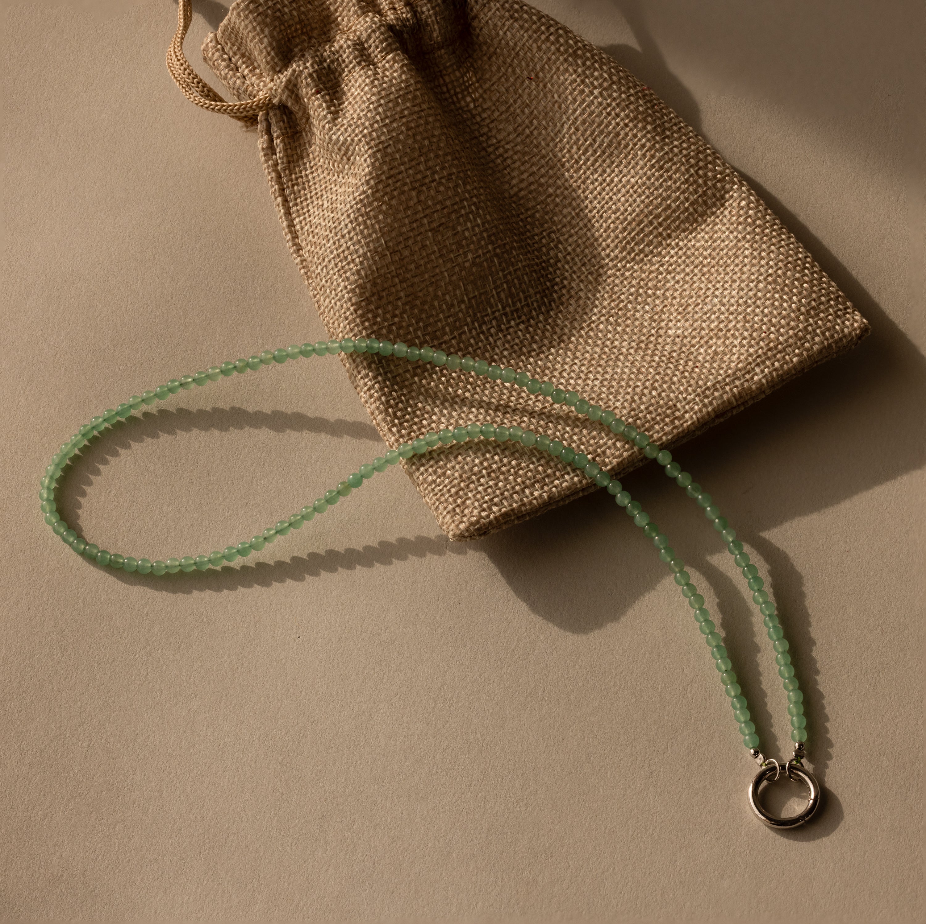 The Beaded Jade Clasp Necklace rests beside a small burlap drawstring pouch.