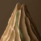 The Beaded Jade Clasp Necklace is draped over a sculpted, textured, beige mountain-like structure.