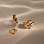 The Mixed Metal Circle Hoops combine gold and silver in two elegant earrings with matching circular charms, shown on a beige surface.
