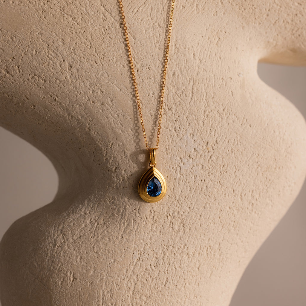 Ribbed Blue Zircon Pendant Necklace with a blue teardrop charm, displayed on a textured beige mannequin bust.