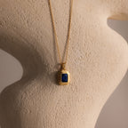 Ribbed Sapphire Pendant Necklace with a ribbed gold chain and a blue rectangular pendant, showcased on a textured beige sculpture.