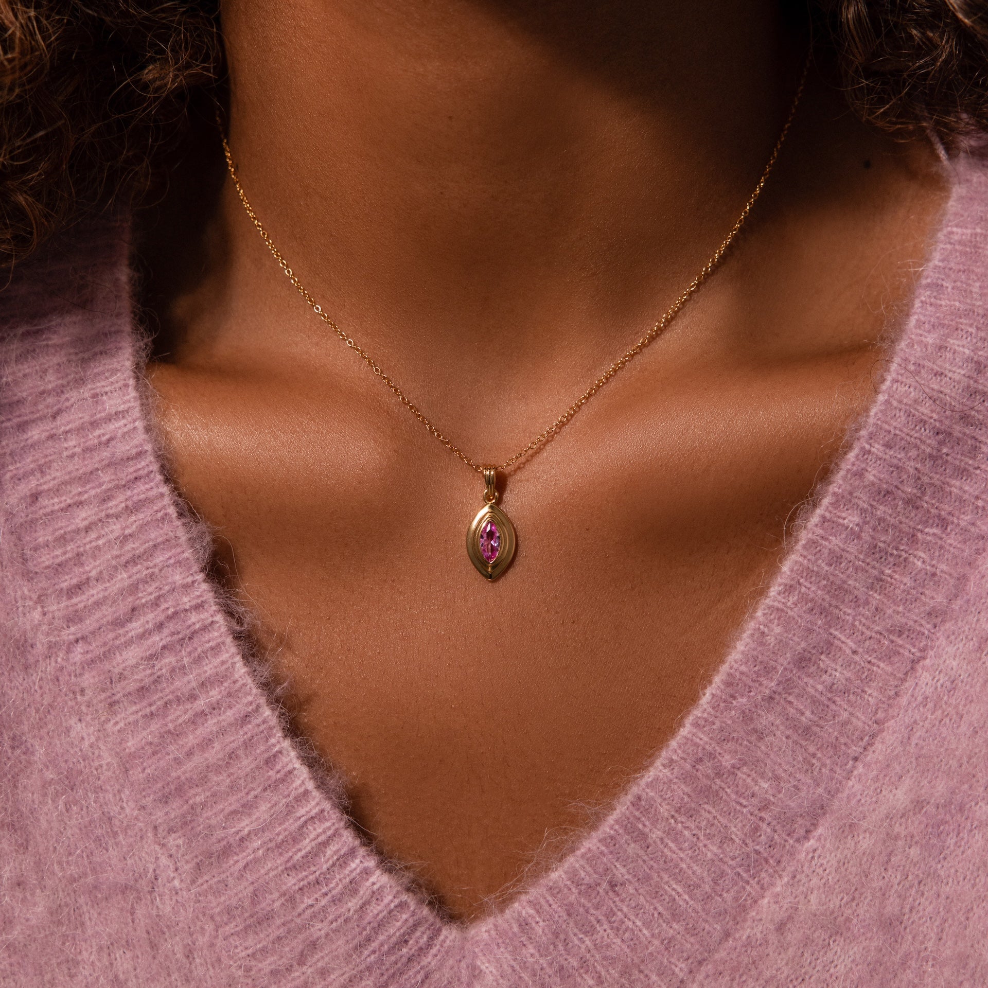 The Ribbed Moonstone Pendant Necklace shines elegantly on a person dressed in a soft lavender V-neck sweater.
