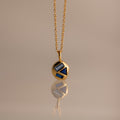 Mixed Sapphire Capsule Pendant Necklace featuring a gold round capsule pendant with geometric blue sapphire inlays, displayed on a neutral background.